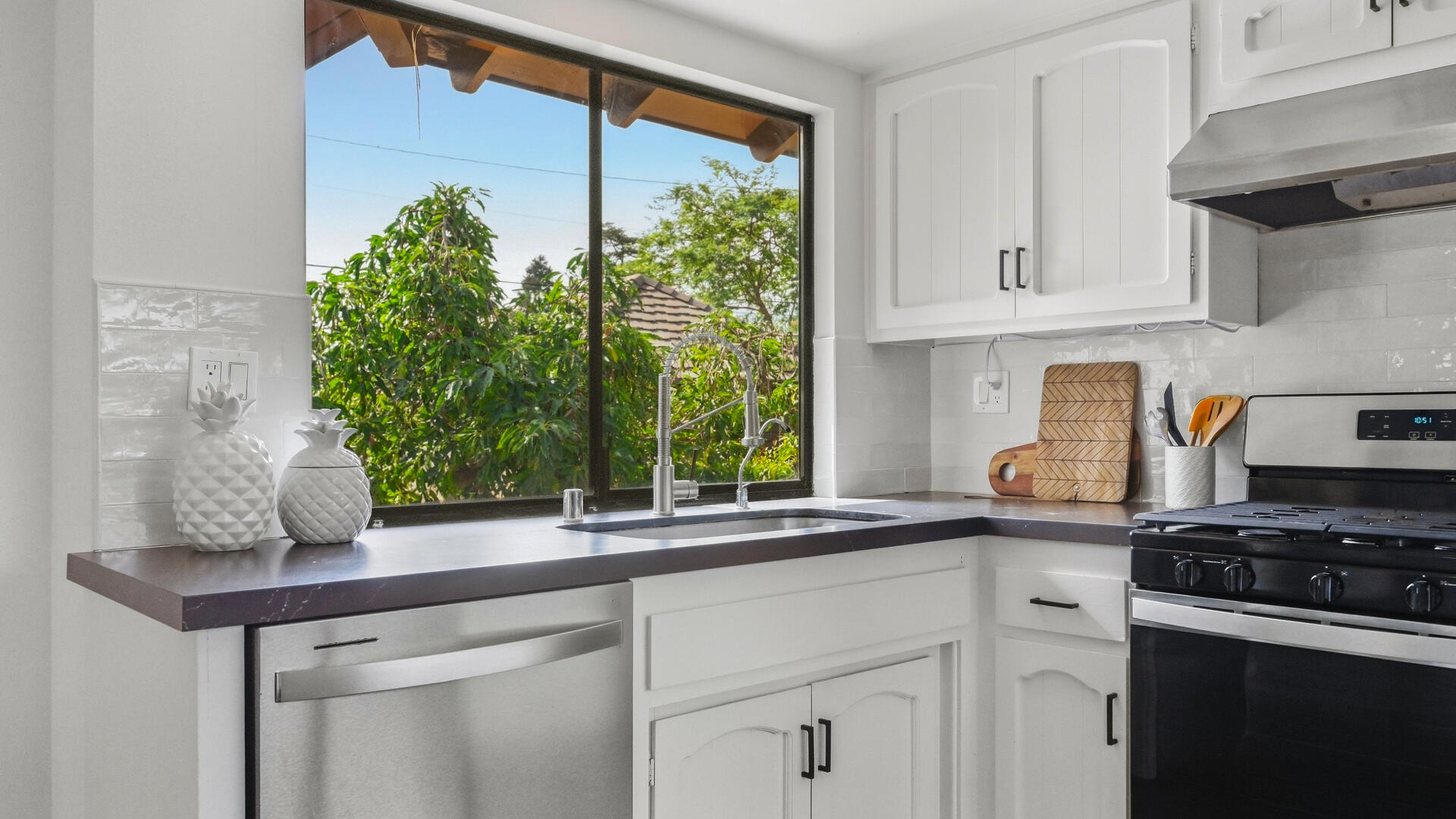 Bright kitchen with white cabinets and a sink beneath a large garden-facing window.