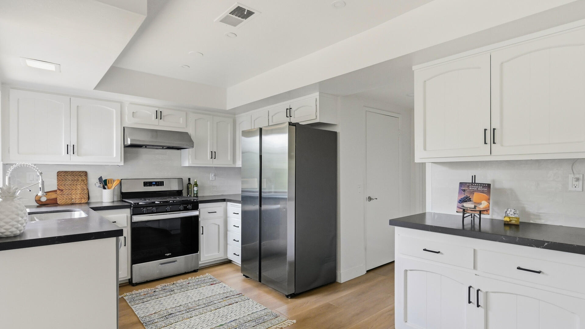 Bright kitchen with white cabinets, dark counters, stainless steel appliances, and light wood floors.