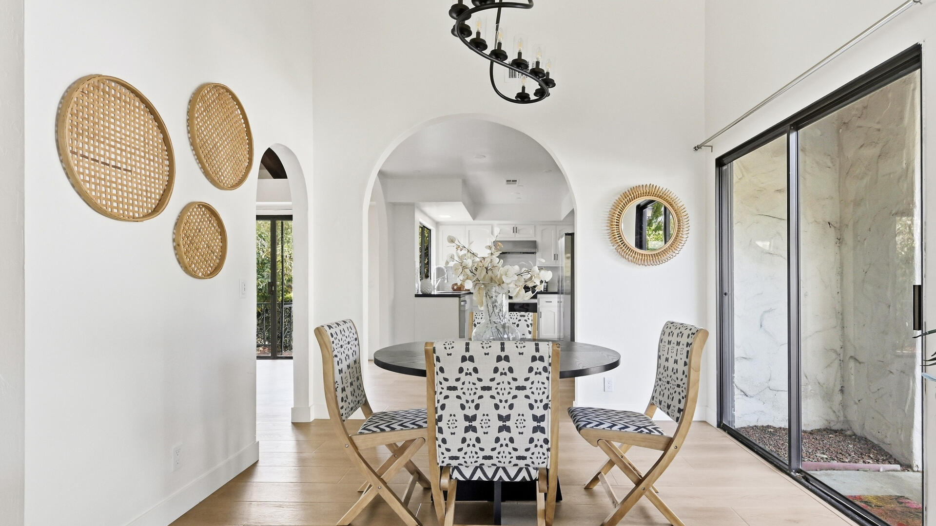 Dining area with a round table and patterned chairs, an arched opening to the kitchen, and a sliding glass door.