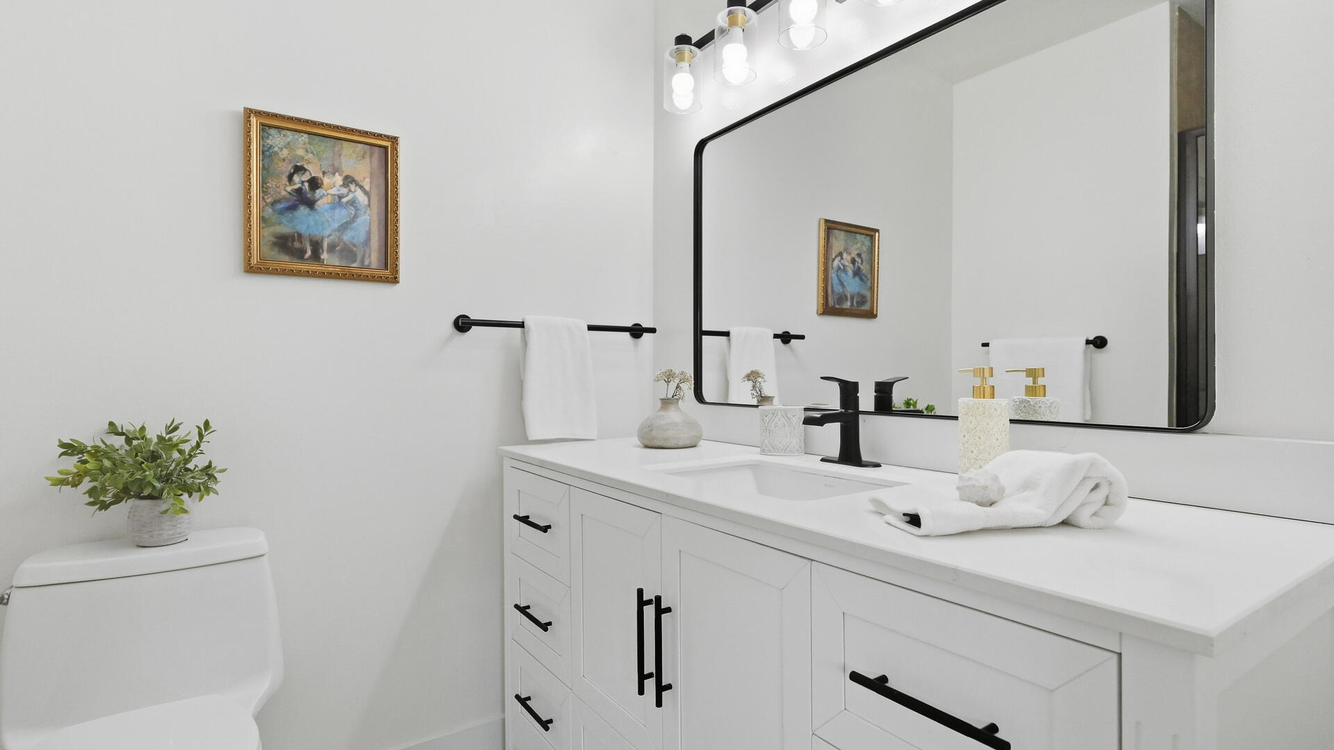 Bright bathroom with a white vanity, black hardware, and a large mirror.