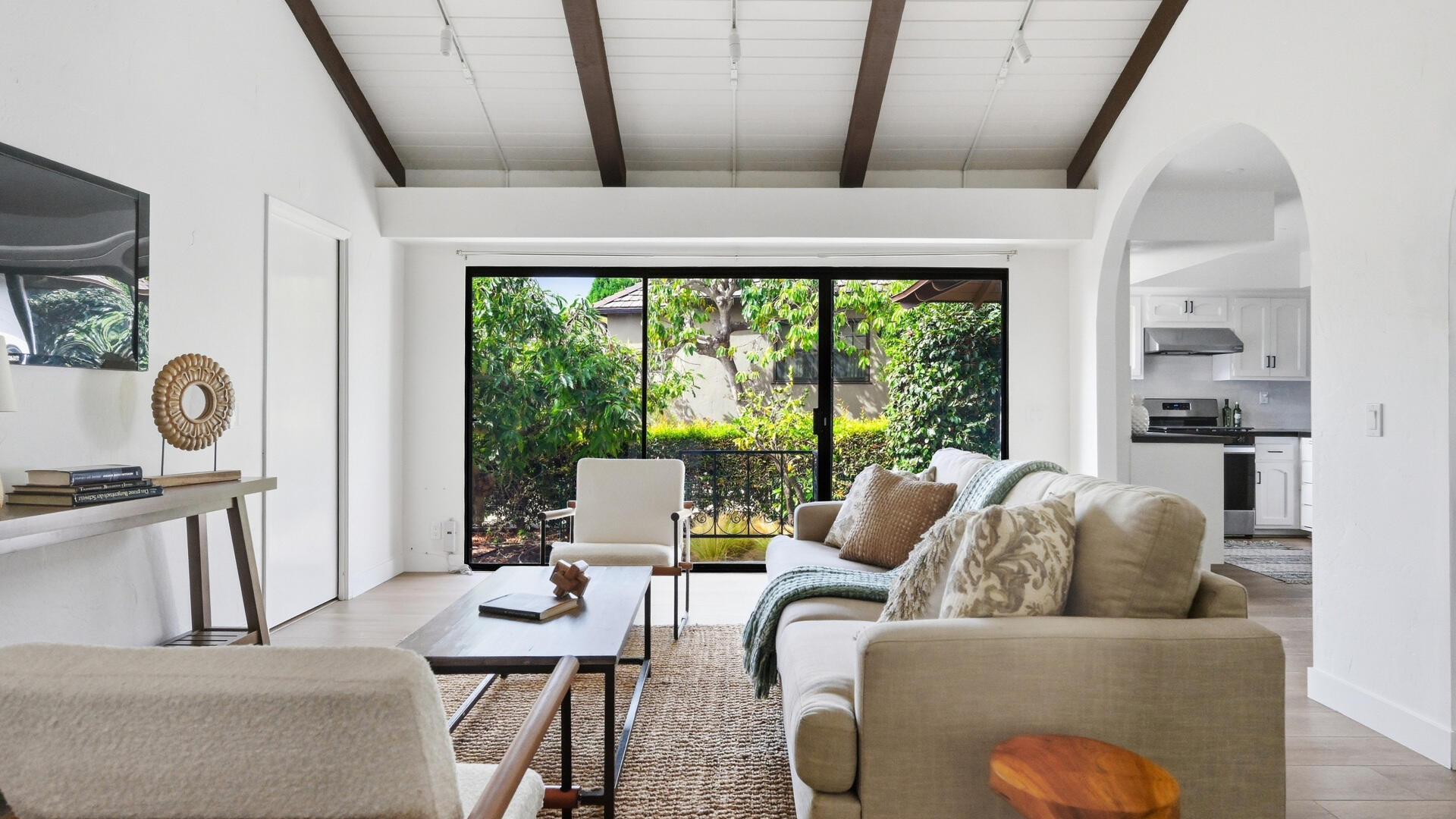 Living room with a vaulted beamed ceiling, neutral seating, and sliding glass doors overlooking a garden.