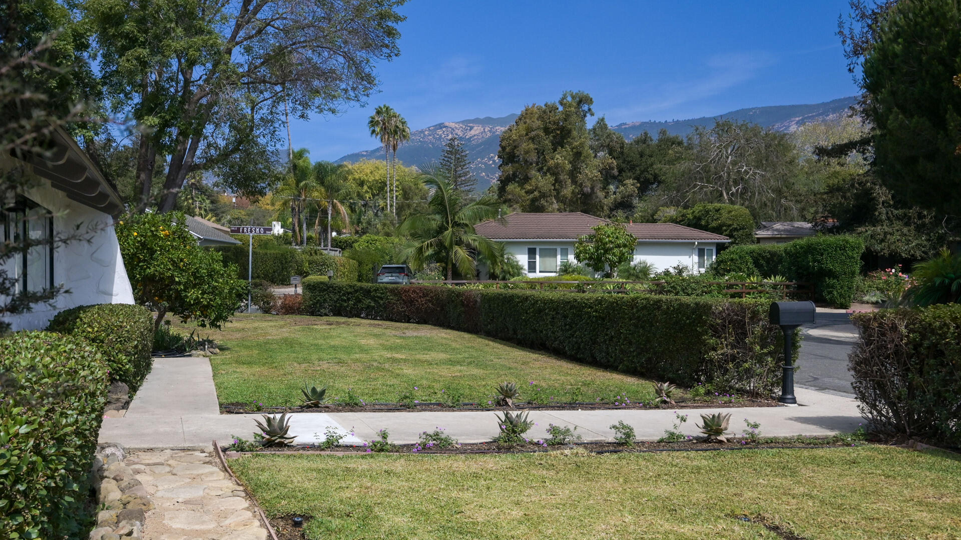 Single-story white house beyond a landscaped lawn, with mountains rising behind it.