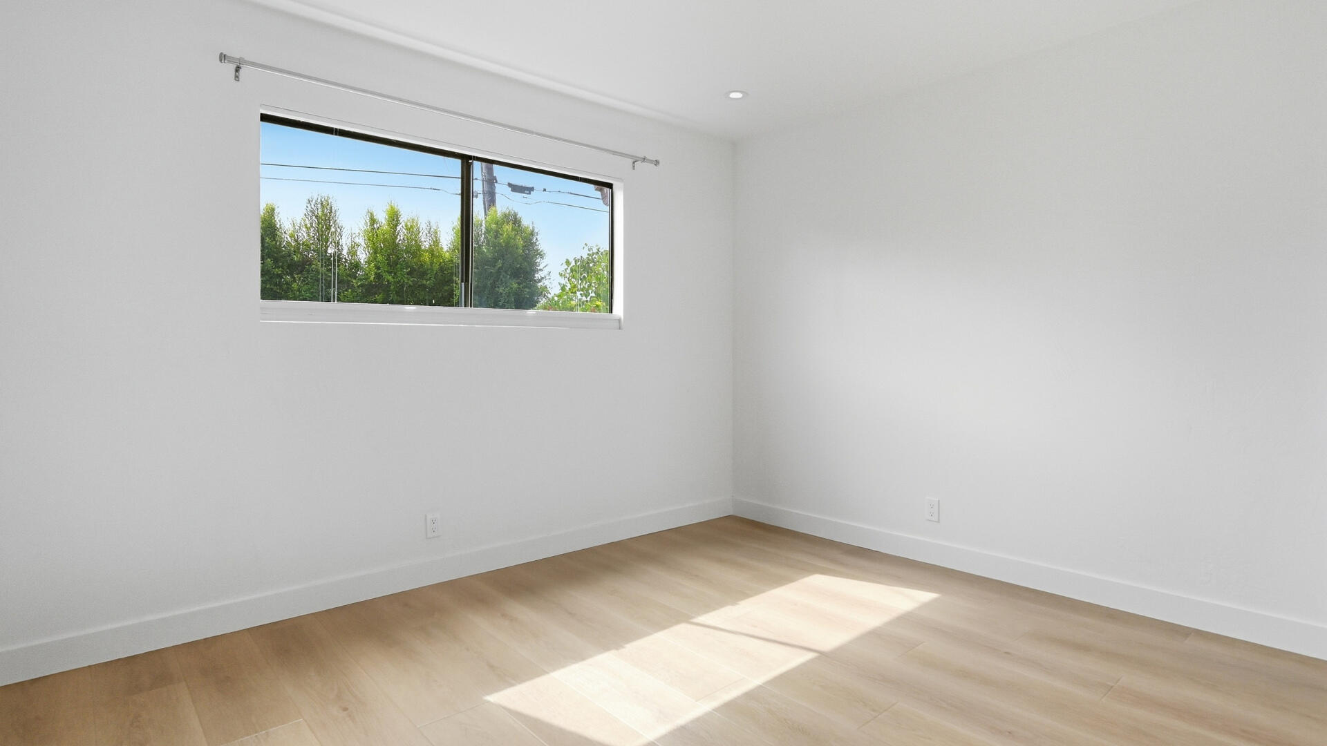 Empty room with light wood flooring and a wide window overlooking greenery.