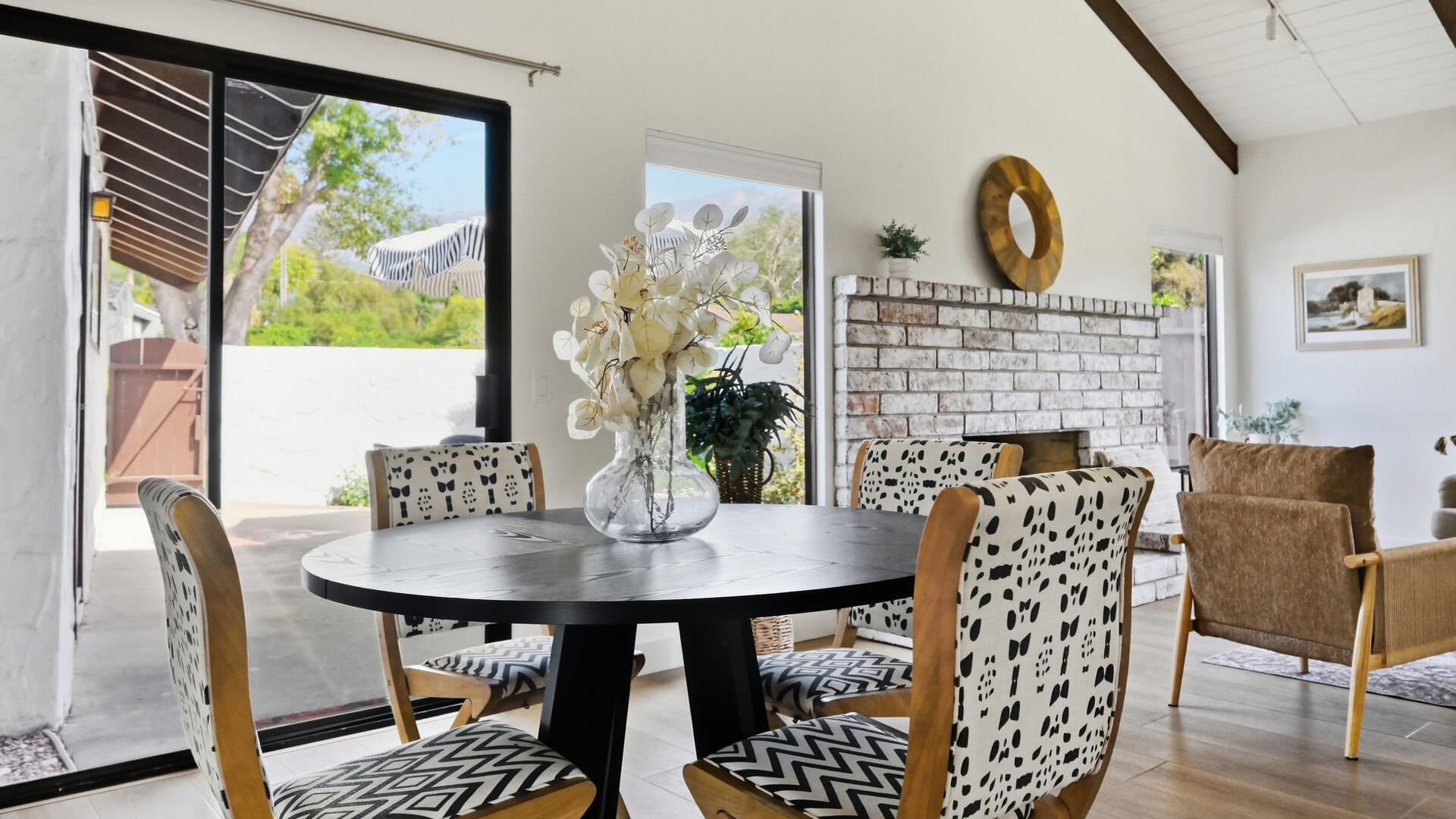 Dining area with a round black table beside a white brick fireplace and patio doors.