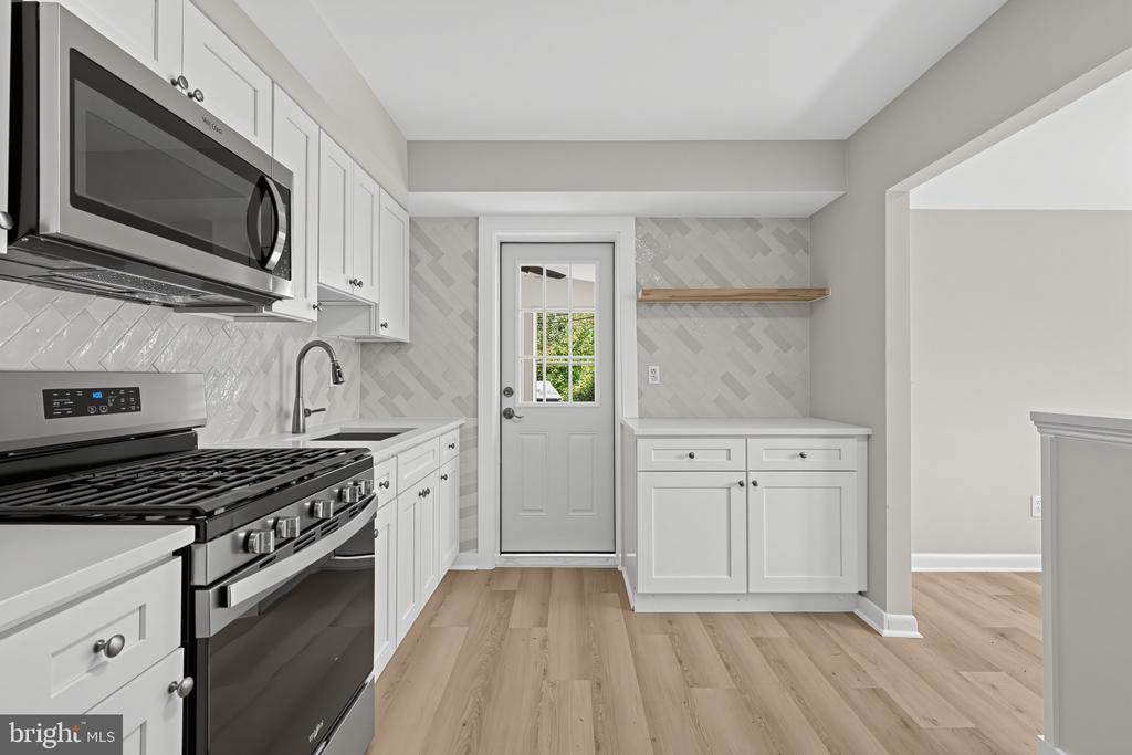 Kitchen with white cabinets, stainless appliances, patterned tile backsplash, and light wood floors.