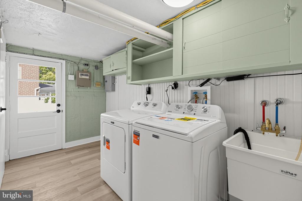 Laundry room with washer, dryer, pale green cabinets, and a utility sink.