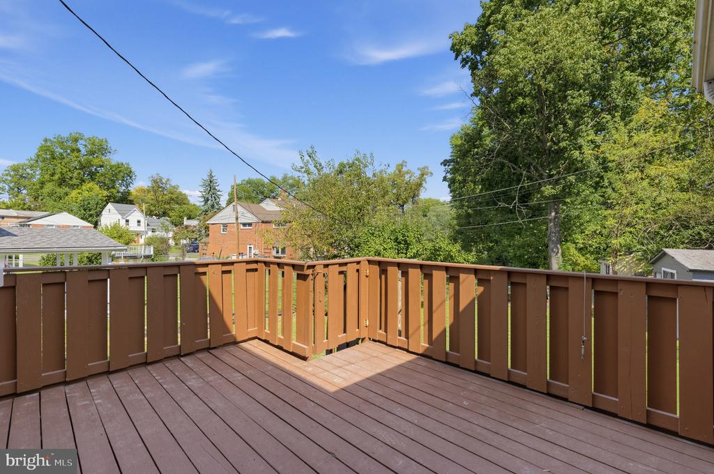 Wooden deck with brown railings overlooking leafy trees and neighboring homes.