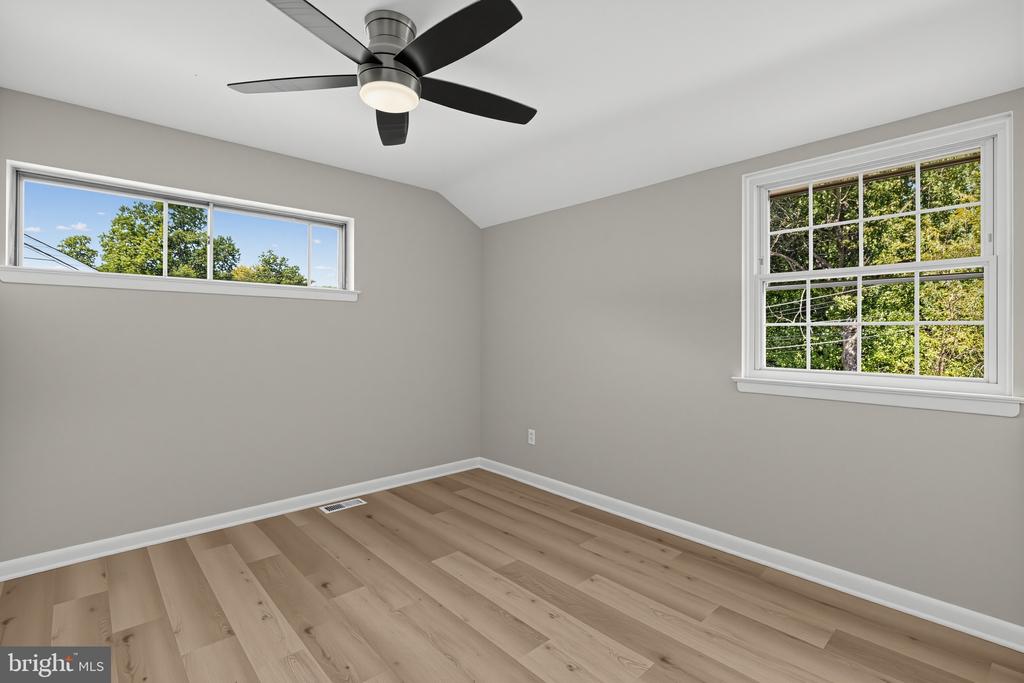 Empty bedroom with wide-plank wood flooring, a black ceiling fan, and two windows.