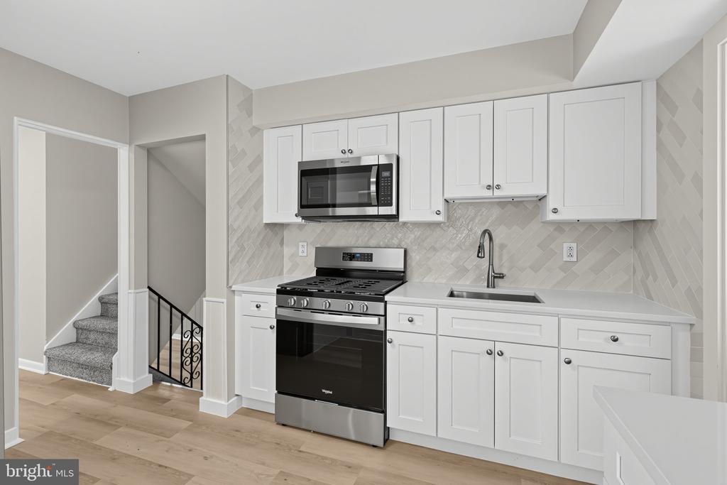 Kitchen with white cabinets, stainless steel appliances, herringbone backsplash, and an adjacent carpeted staircase.