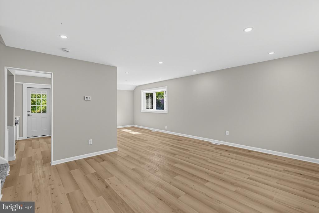 Vacant living room with light wood floors, recessed lighting, and a window.