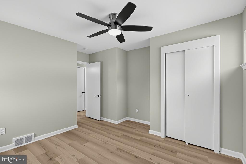 Empty bedroom with light wood flooring, a black ceiling fan, and a white sliding-door closet.