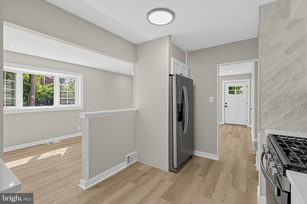 Kitchen with stainless steel appliances, gray walls, light wood flooring, and an adjoining room with a wide window.