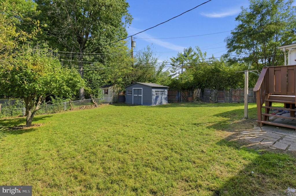 Backyard with a broad lawn, gray shed, mature trees, and deck steps.