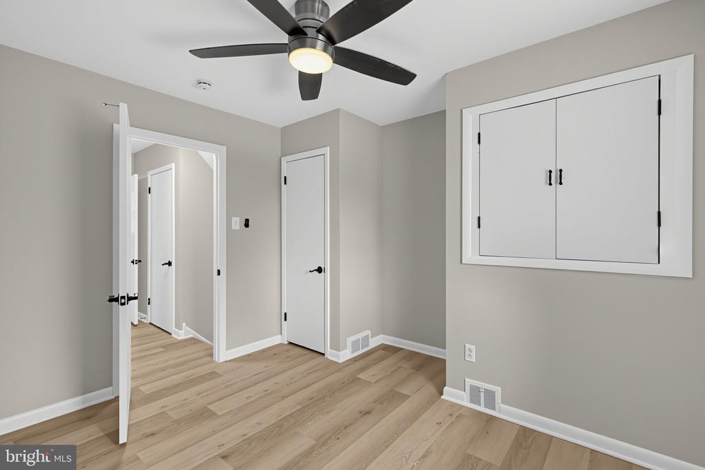 Empty room with light wood-look flooring, a black ceiling fan, and a large built-in closet.
