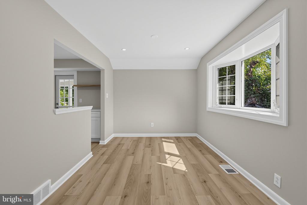 Empty room with light wood floors, neutral walls, and a large window overlooking greenery.