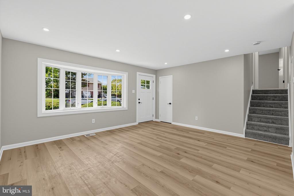 Vacant room with light wood flooring, a large window, two doors, and carpeted stairs.