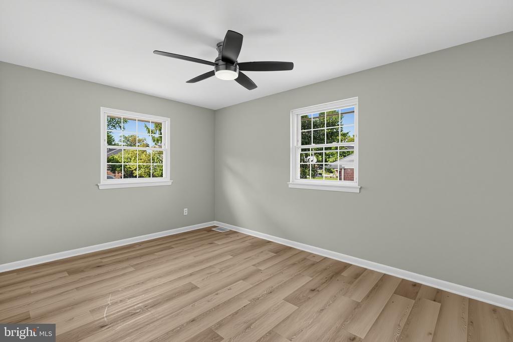 Empty room with wood-look flooring, two windows, gray walls, and a black ceiling fan.