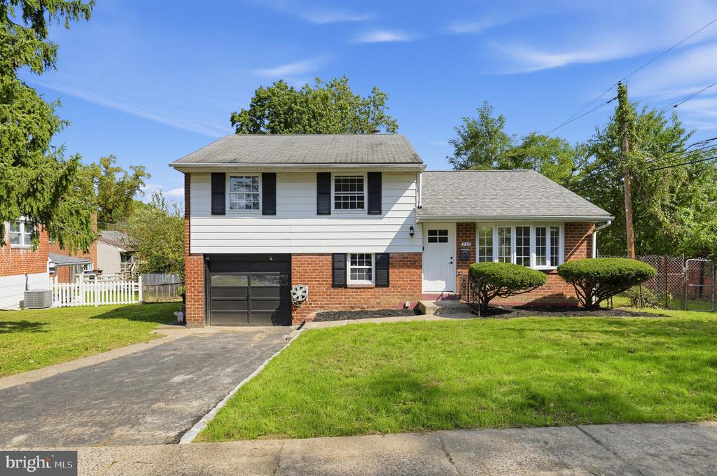 Split-level house with white siding, red brick, a dark garage, and a broad front lawn.