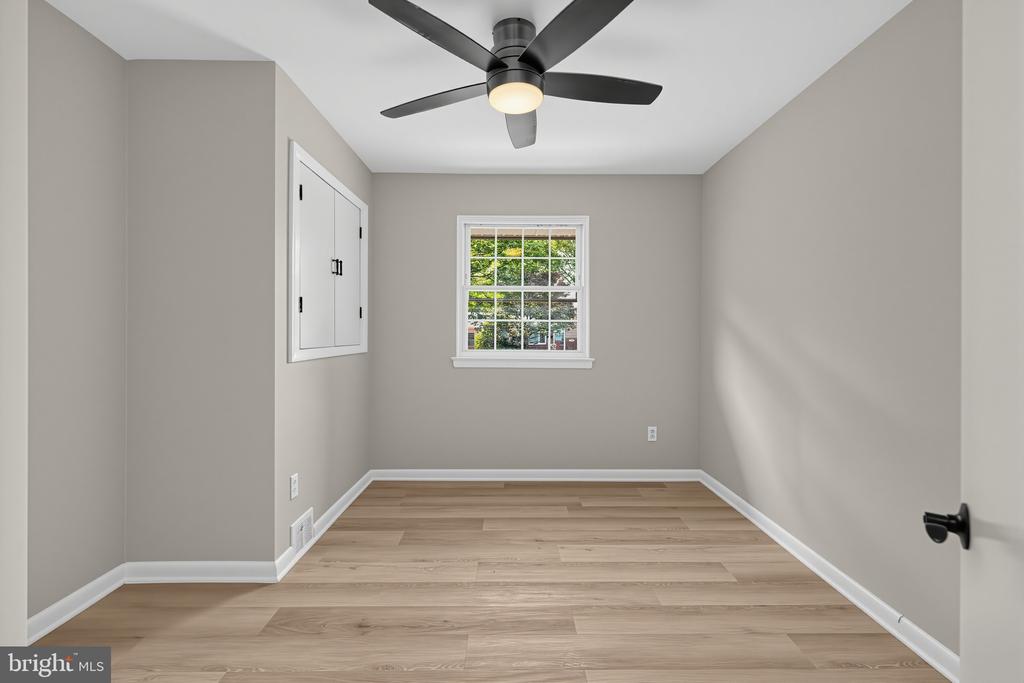 Vacant bedroom with light wood flooring, a black ceiling fan, and a white-trimmed window.