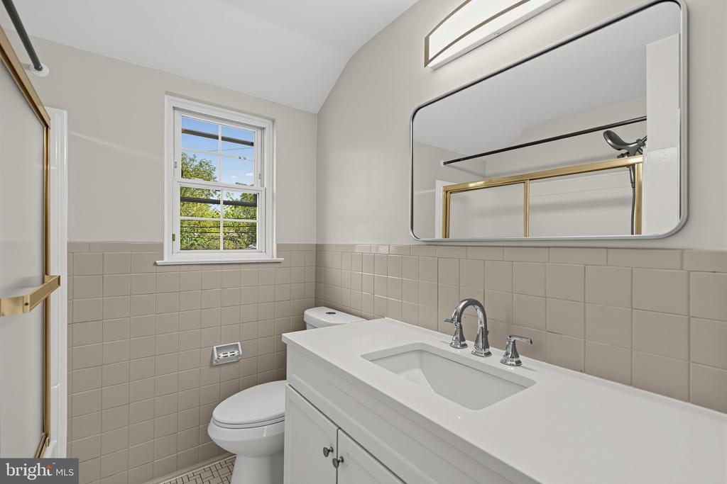 Bathroom with a white vanity, large mirror, tiled walls, and a window.