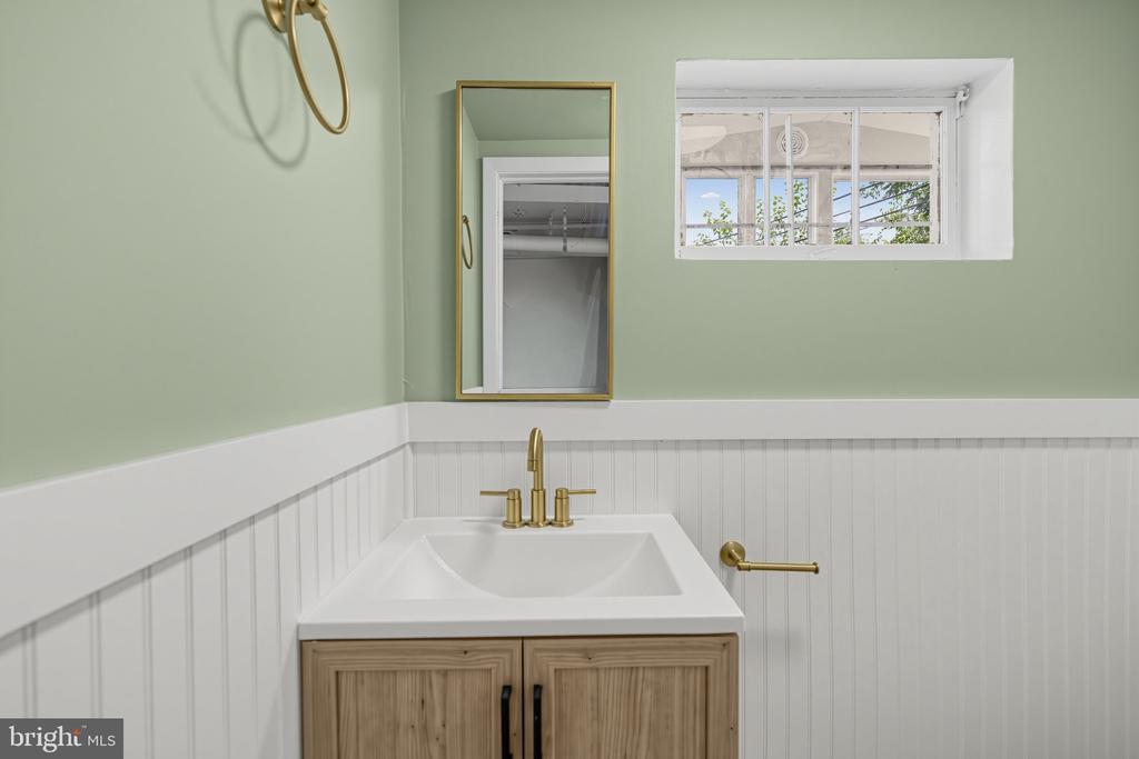 Bathroom with a light wood vanity, brass fixtures, sage walls, and white beadboard wainscoting.