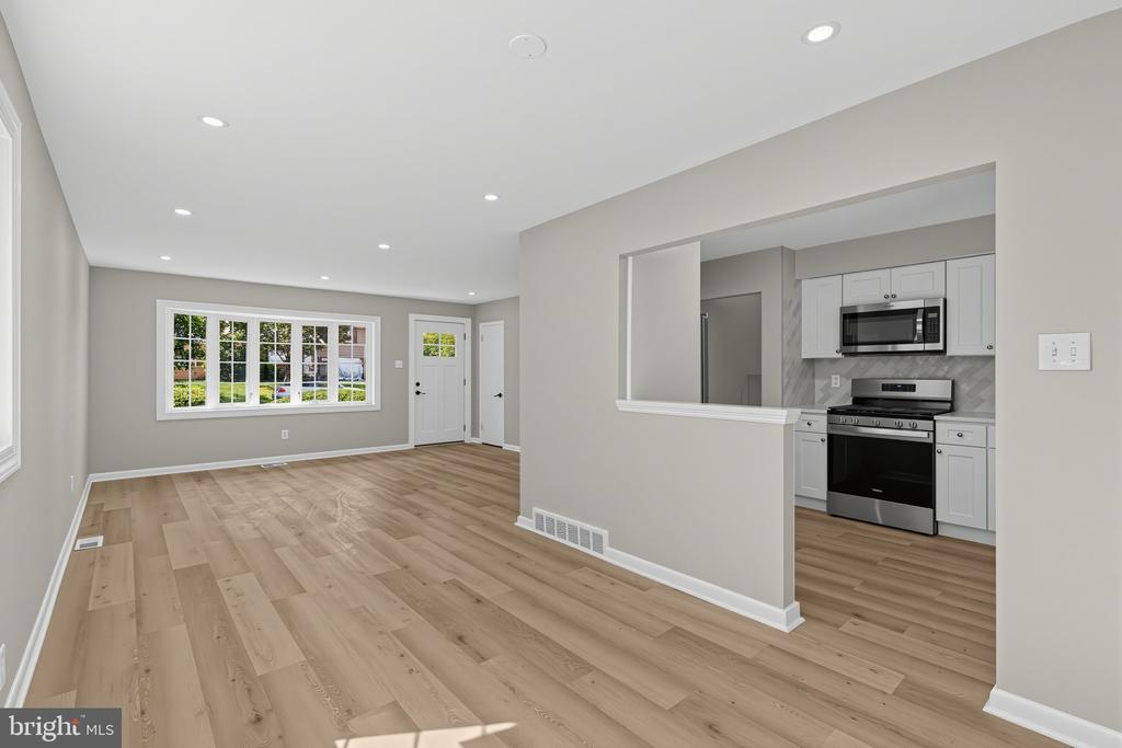 Vacant living room with wood-look flooring, recessed lights, and a pass-through to the kitchen.