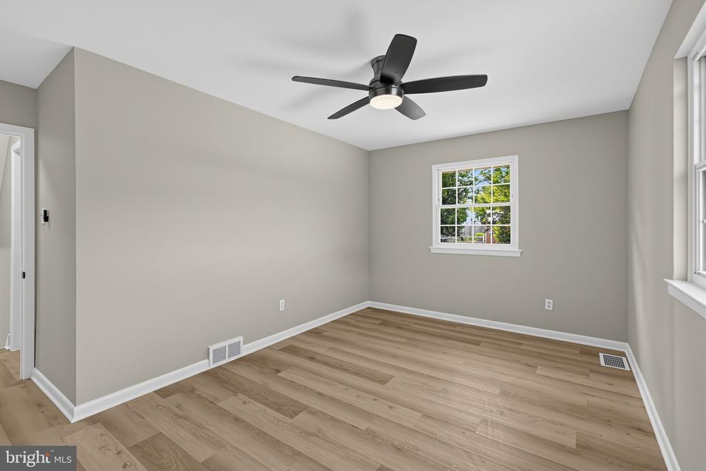 Empty room with gray walls, light wood flooring, a black ceiling fan, and two windows.