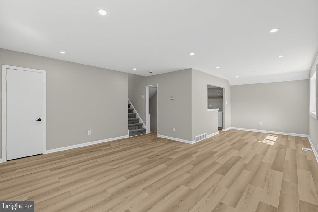 Vacant finished room with light plank flooring, recessed lights, and stairs.