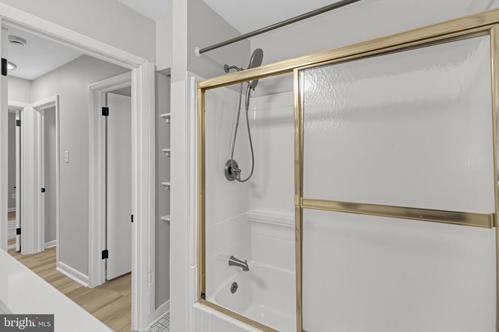 Bathroom with a white tub and shower behind gold-framed sliding glass doors.