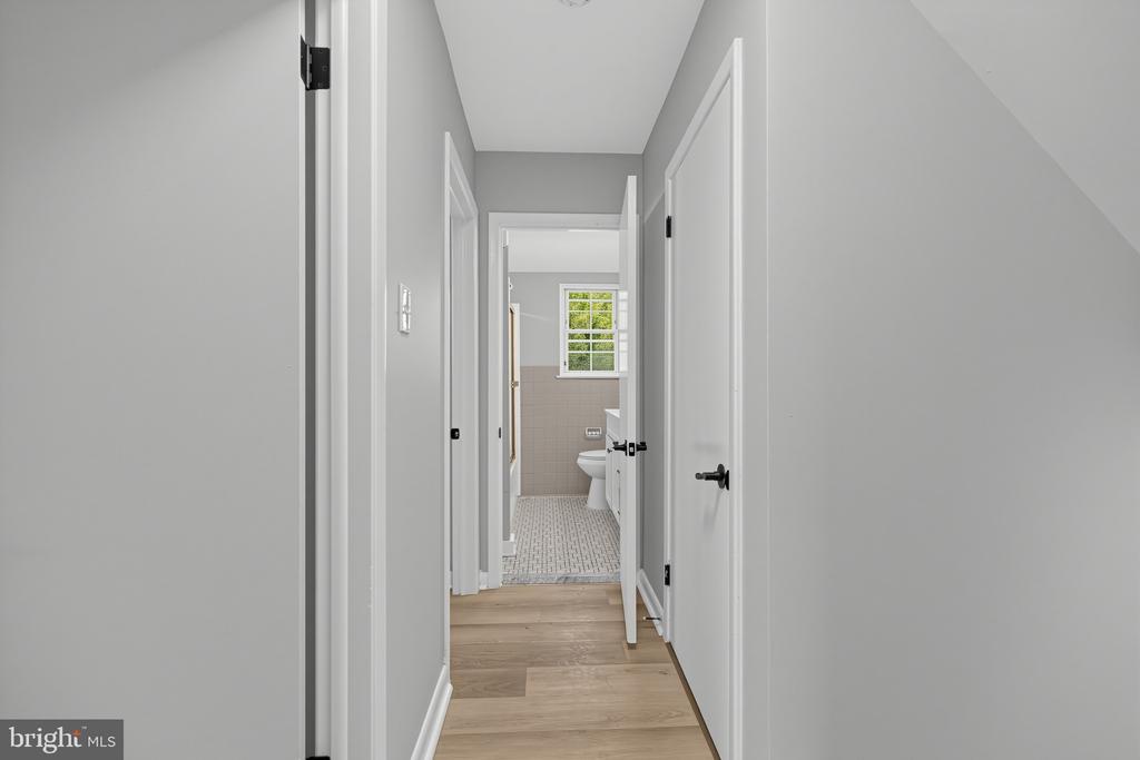Hallway leading to a bathroom, with wood-look flooring and a window.