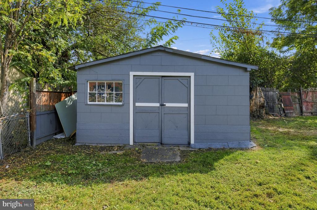 Gray backyard shed with double doors and a small window, surrounded by trees and fencing.