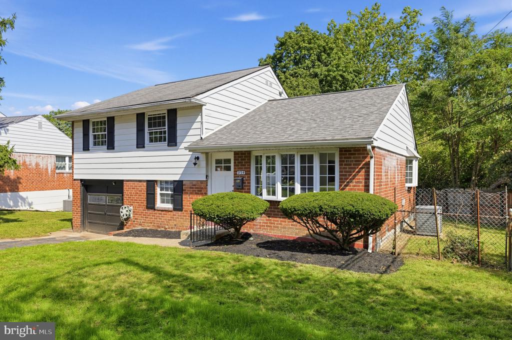 Split-level home with white siding, red brick, black shutters, and an attached garage.