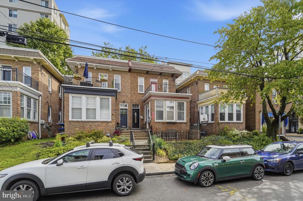 Brick Ardmore rowhouses with front steps, small landscaped yards, mature trees, and cars parked along the street.