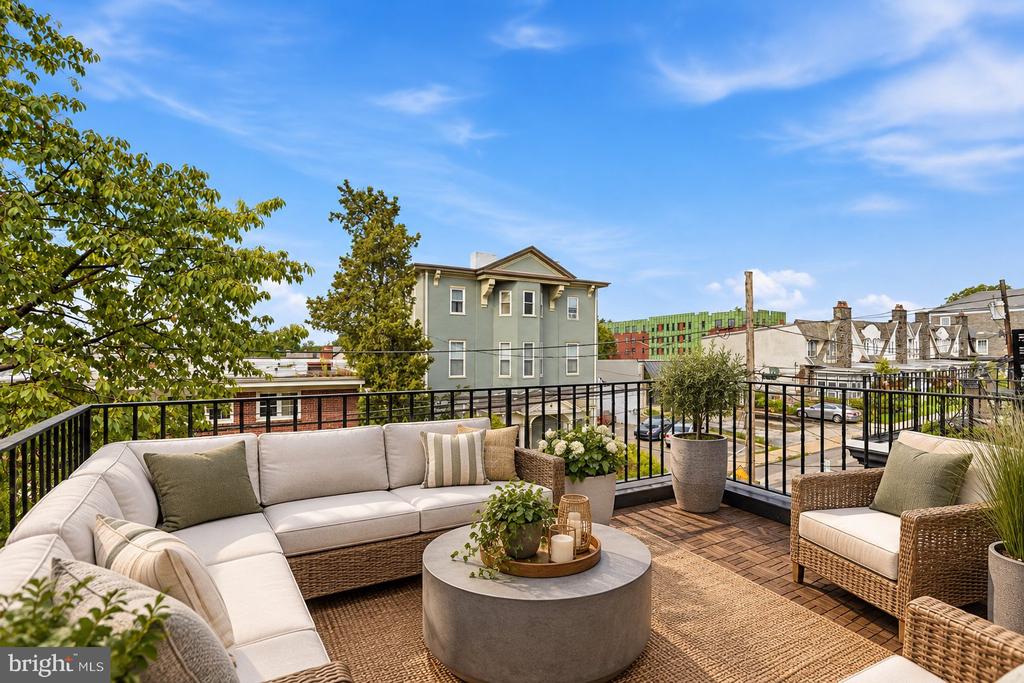 Furnished rooftop terrace with sectional seating, woven chairs, and neighborhood views.