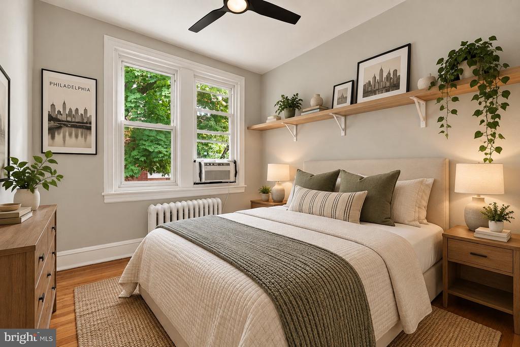 Bedroom with a neatly made bed, leafy window views, and Philadelphia prints above the bed.
