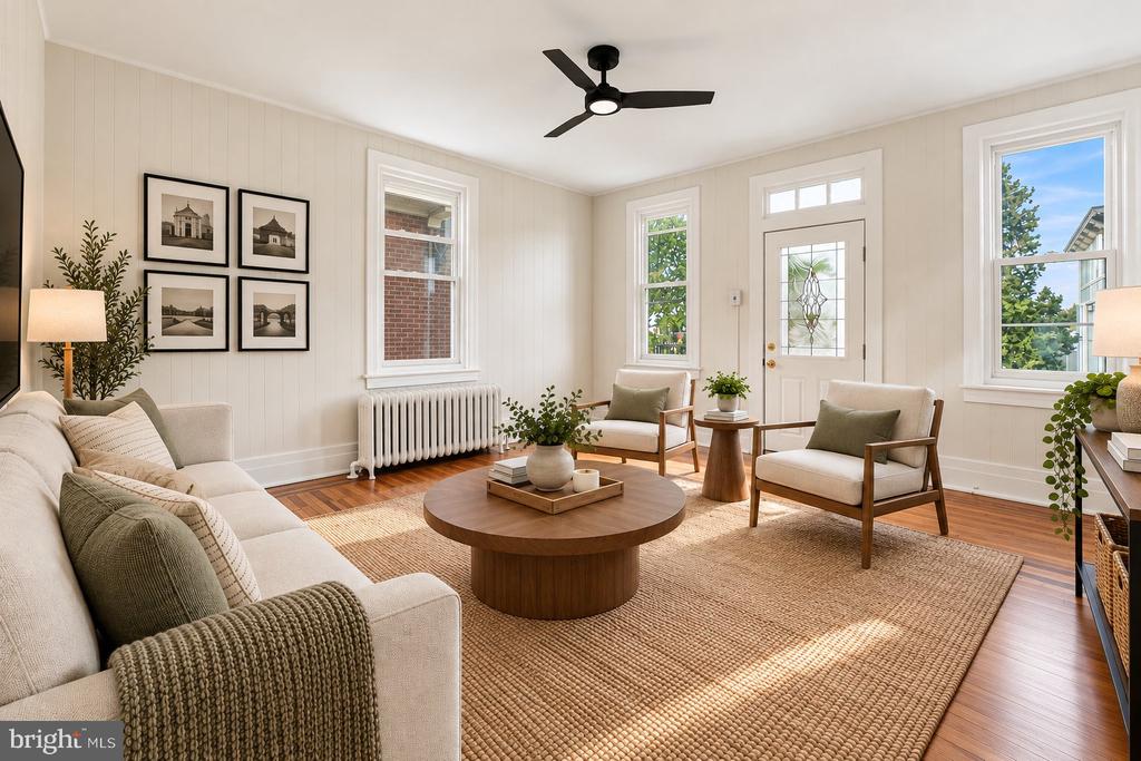 Staged living room with cream seating, a round wood coffee table, and tall windows.