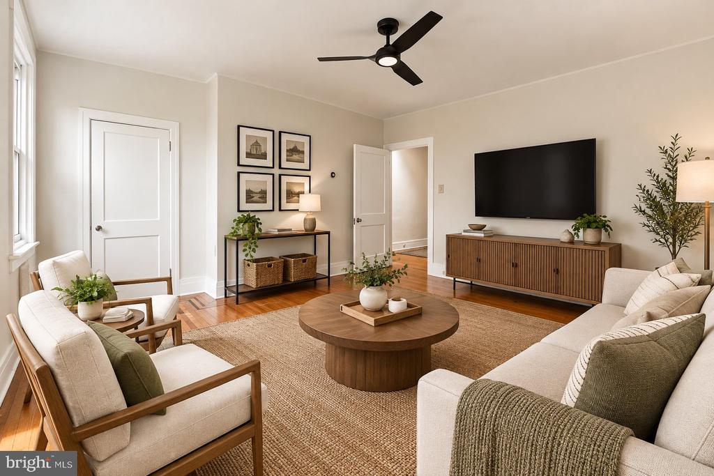 Living room with a round coffee table, cream seating, a wall-mounted TV, and a ceiling fan.