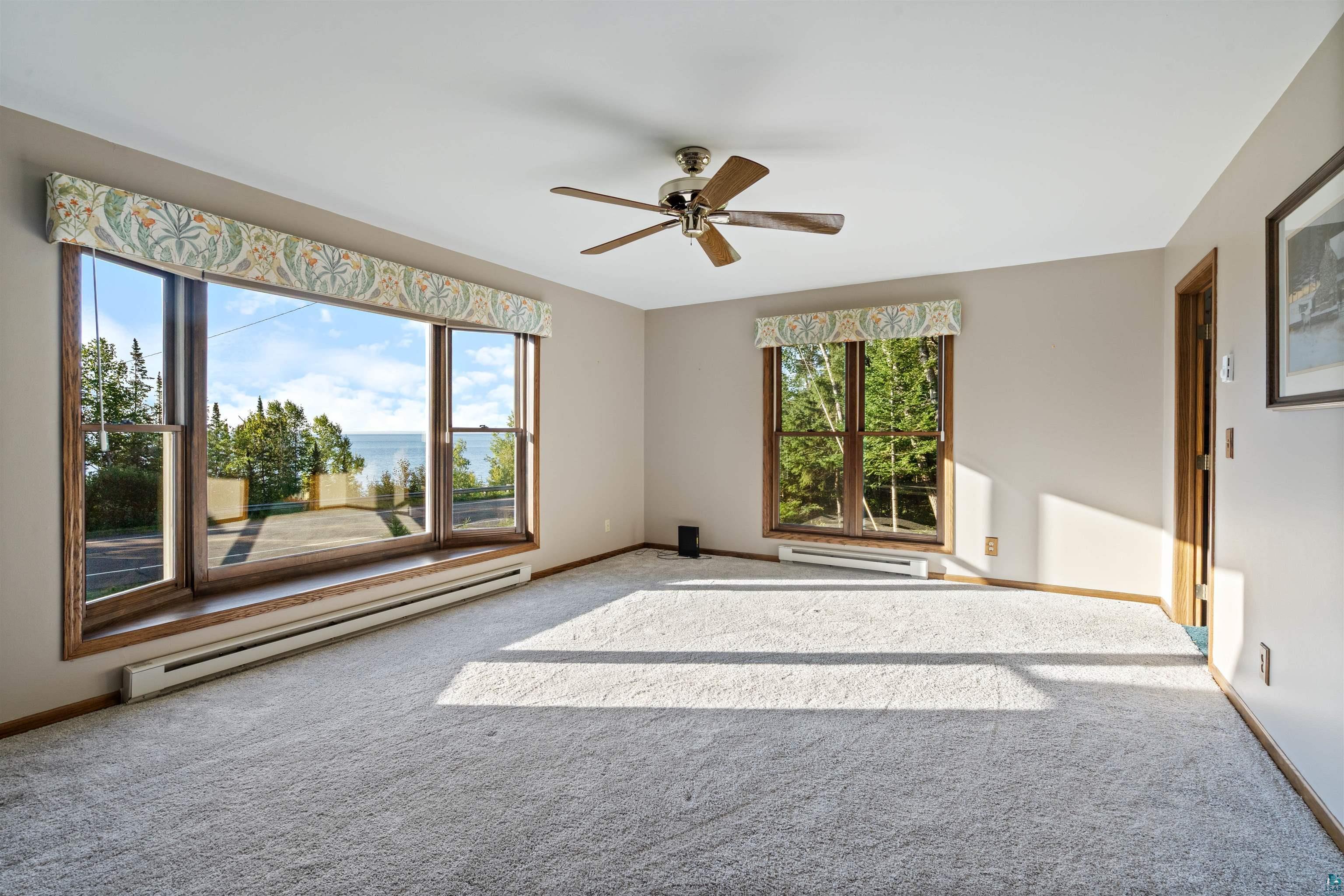 Vacant living room with large windows overlooking Lake Superior and a wood-bladed ceiling fan.