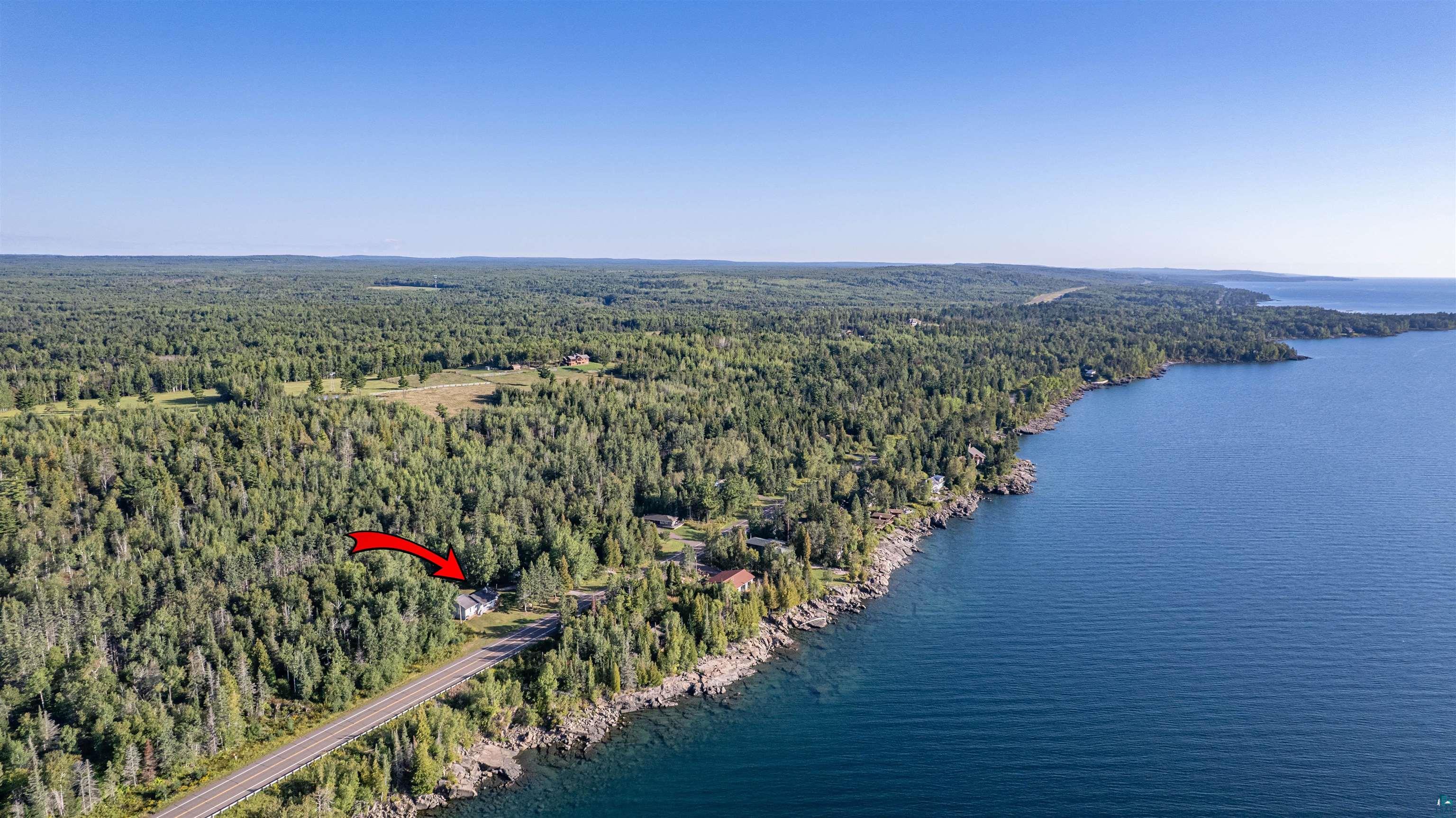 Aerial view of the property marked by a red arrow, amid wooded shoreline beside Lake Superior.