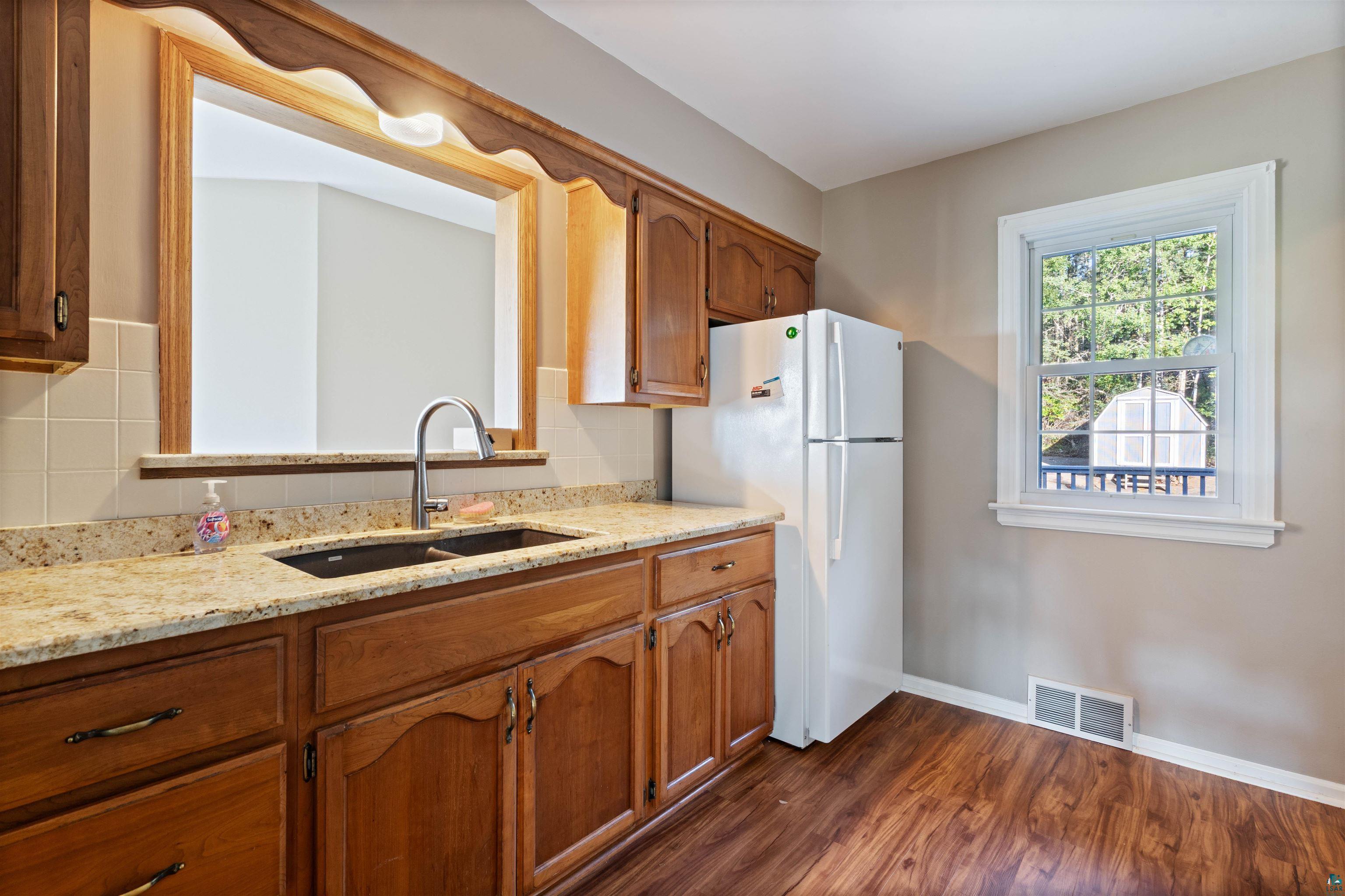 Kitchen with warm wood cabinets, granite counters, a pass-through, and a window facing trees.