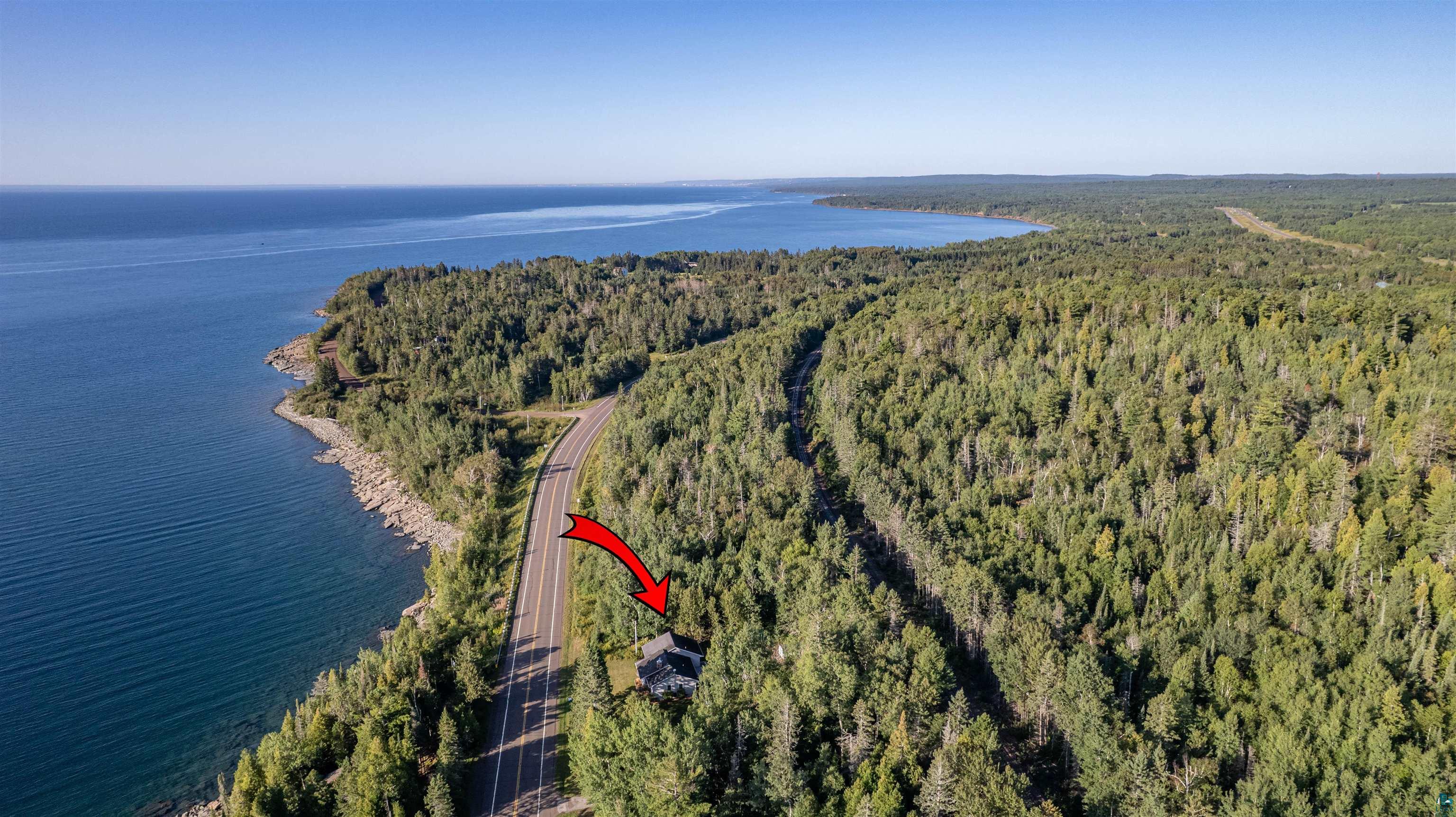 Aerial view of a wooded lakeside home beside a coastal road, marked by a red arrow.