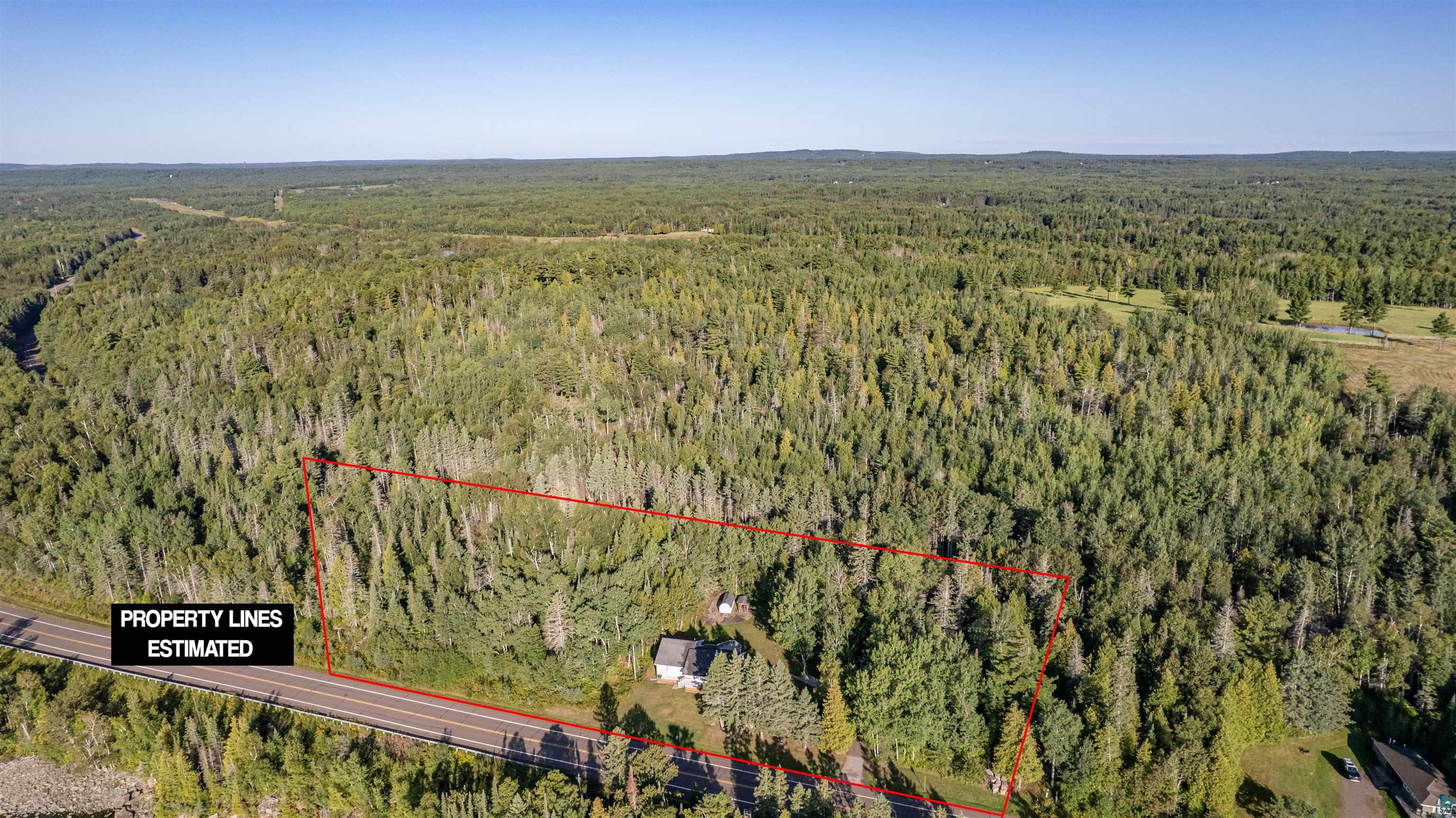 Aerial view of wooded property outlined in red, with a house and road frontage.