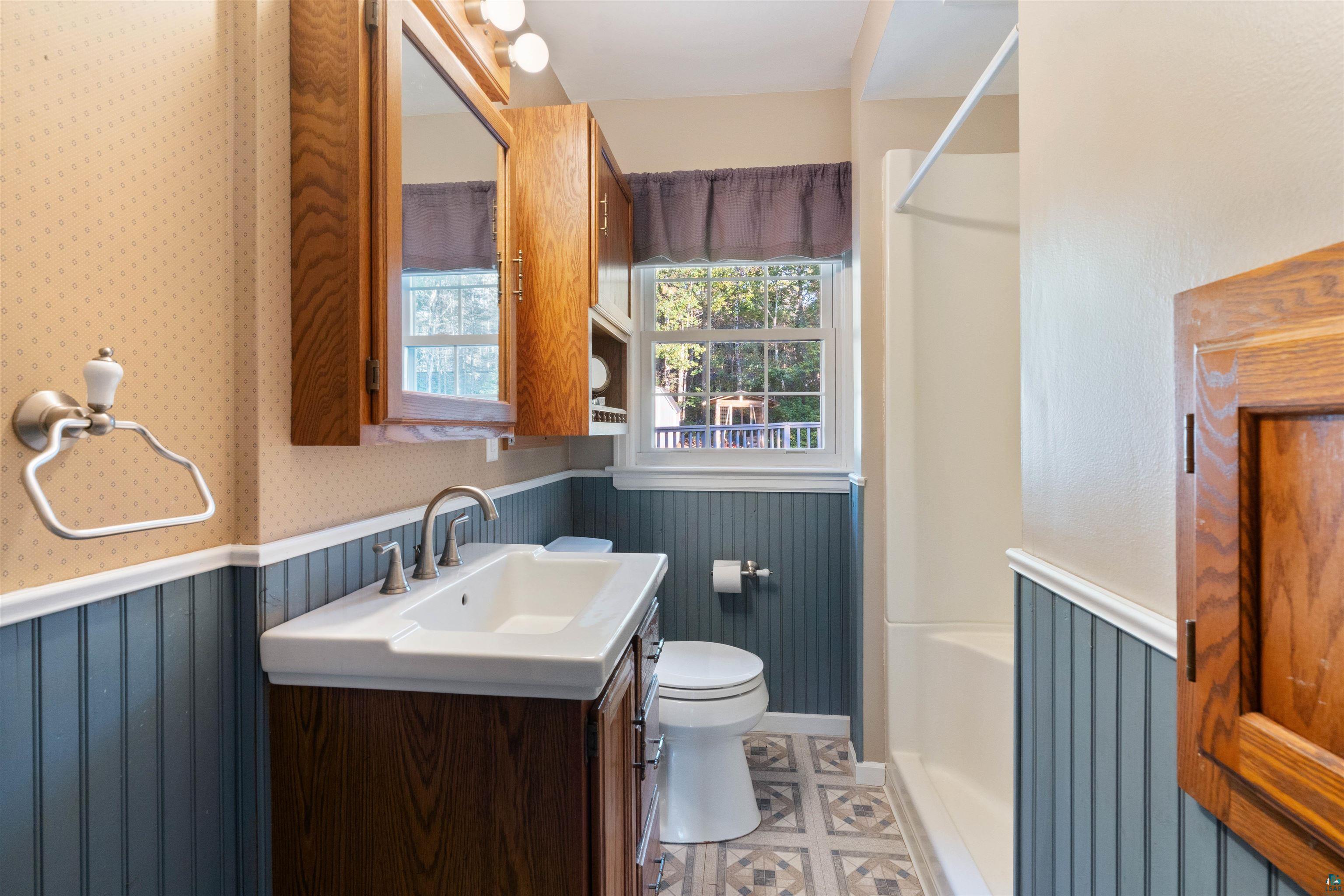 Bathroom with dark wood vanity, blue beadboard wainscoting, and a window overlooking a deck.