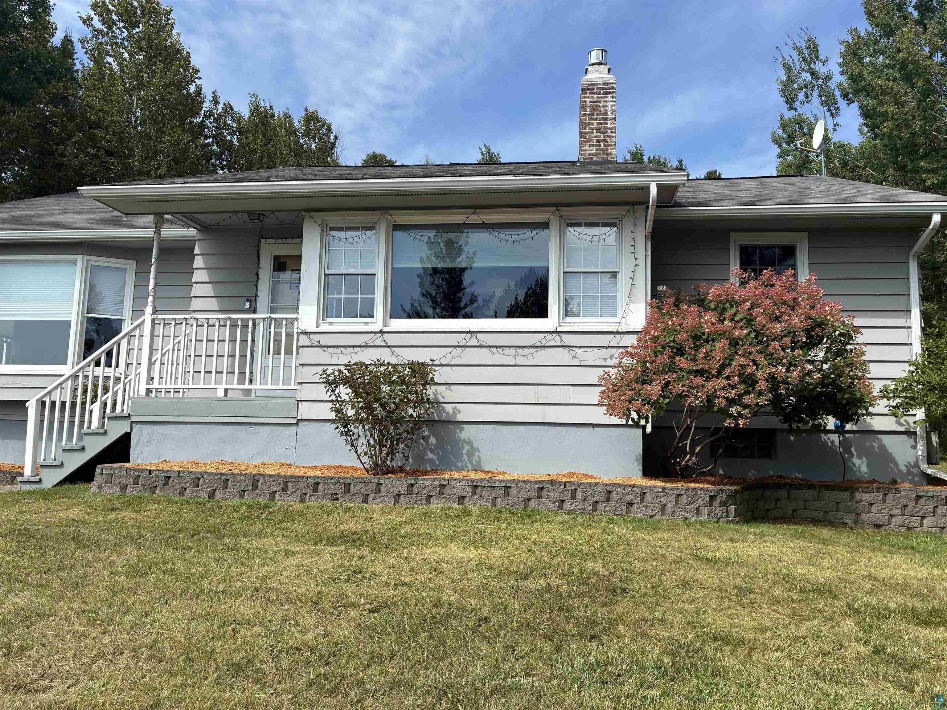 Gray single-story house with white trim, a brick chimney, and a raised entrance with white railings.