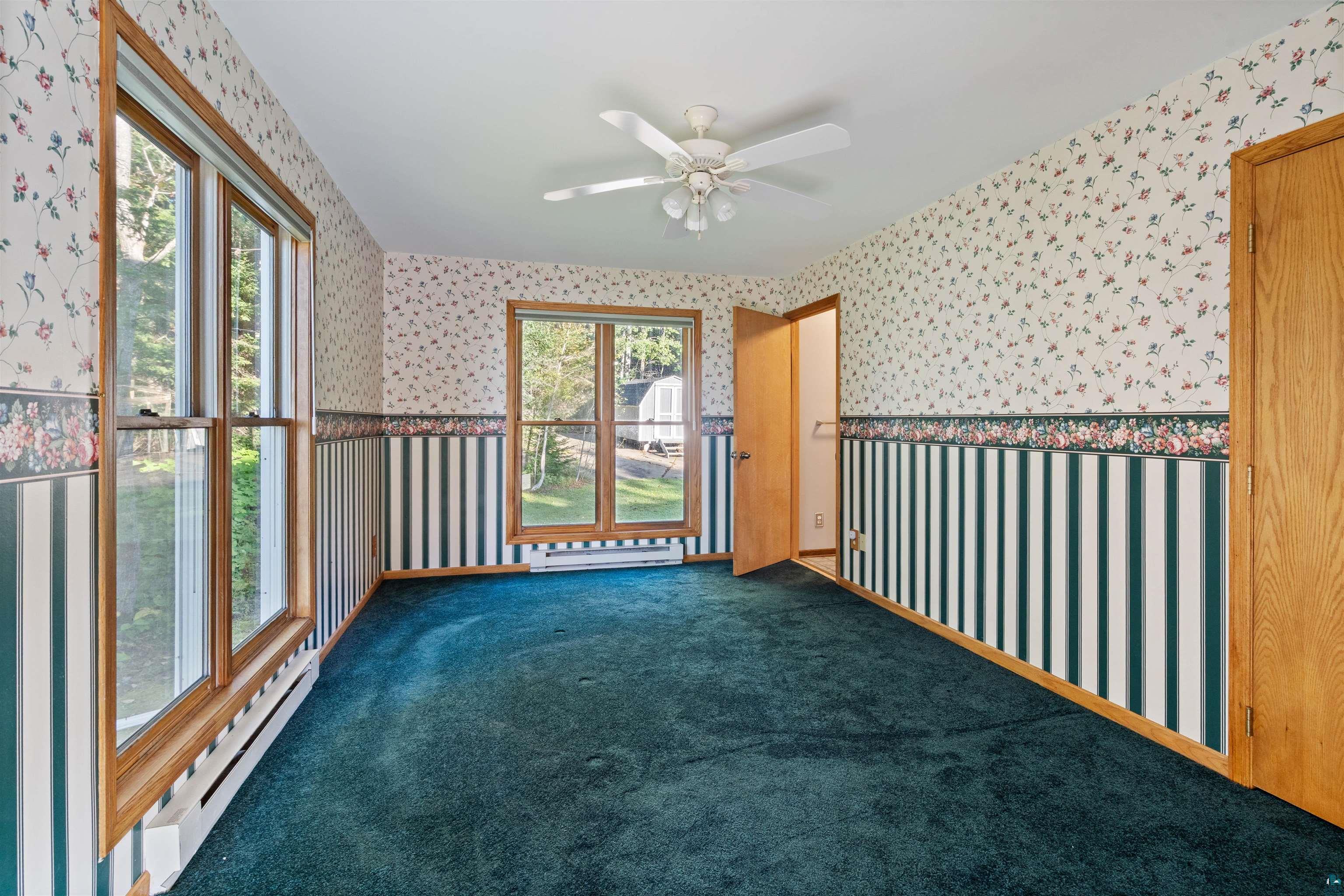 Empty room with blue carpet, floral wallpaper, striped wainscoting, and large wood-trimmed windows.
