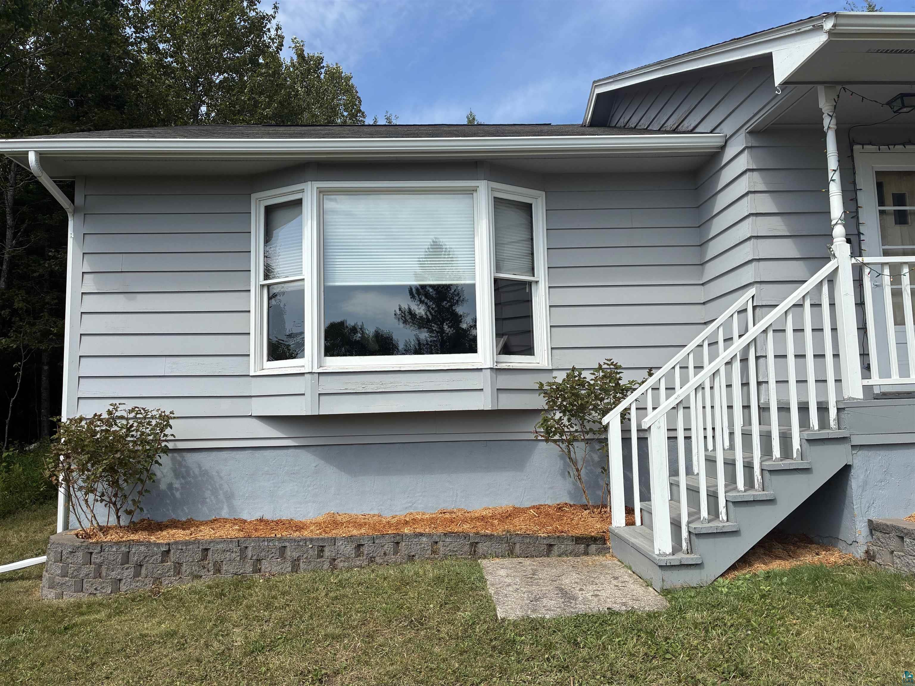 Gray house exterior with a large bay window and white-railed entrance steps.