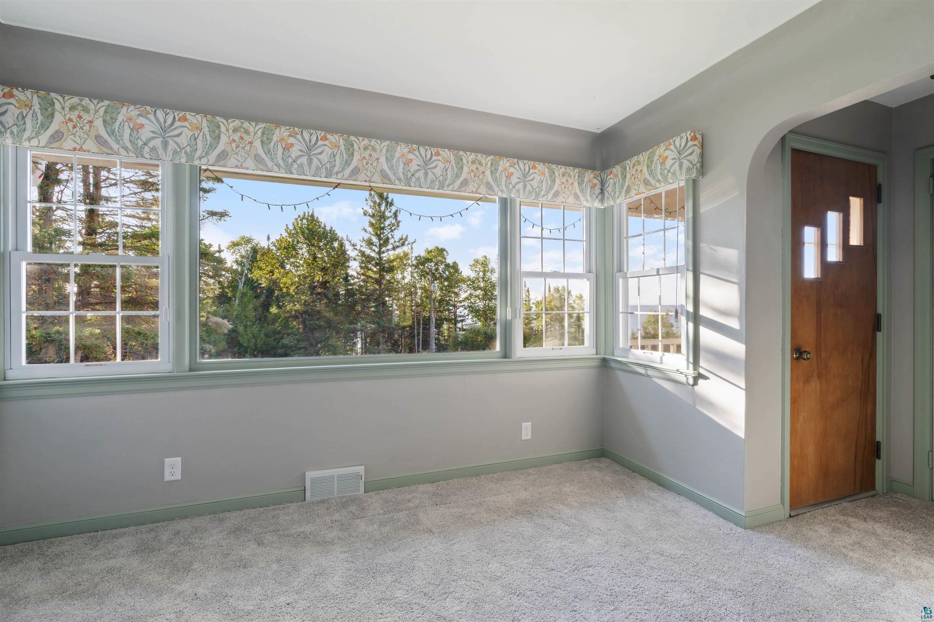 Empty carpeted room with a wide bank of windows overlooking trees and a floral valance.