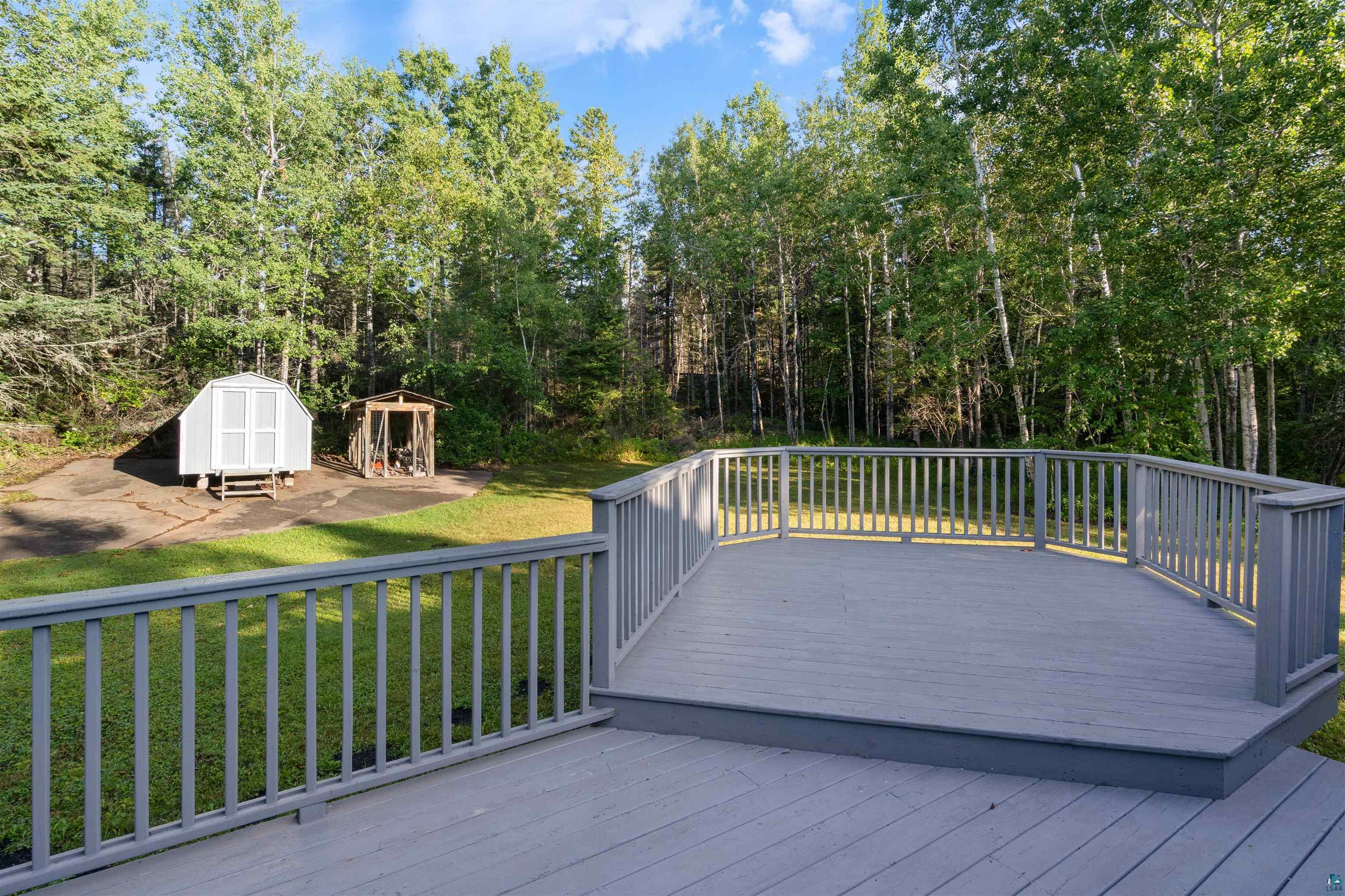 Gray-railed deck overlooking a grassy yard, two sheds, and dense woods.