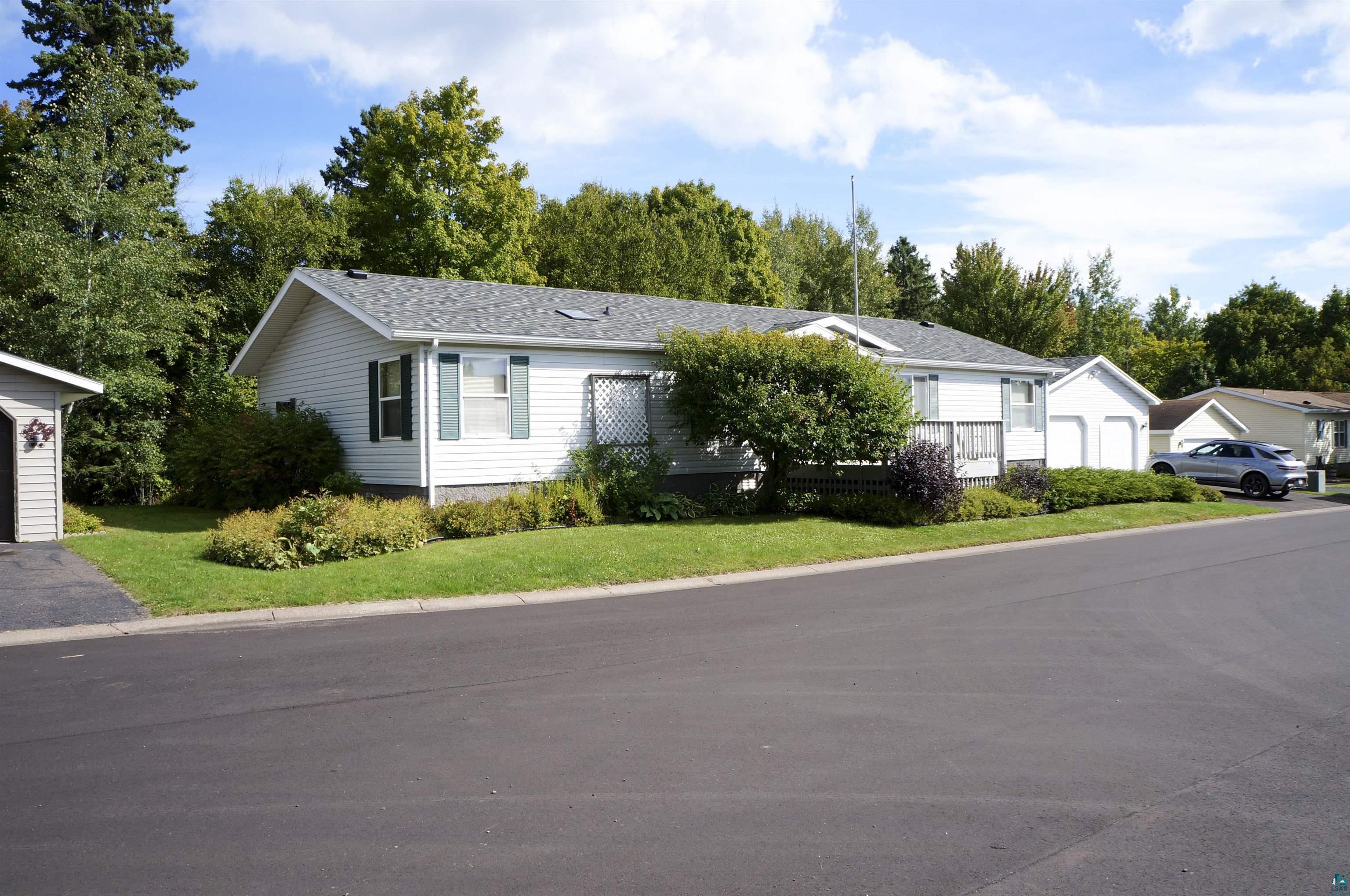 Single-story white home with teal shutters, landscaped shrubs, and an attached garage.