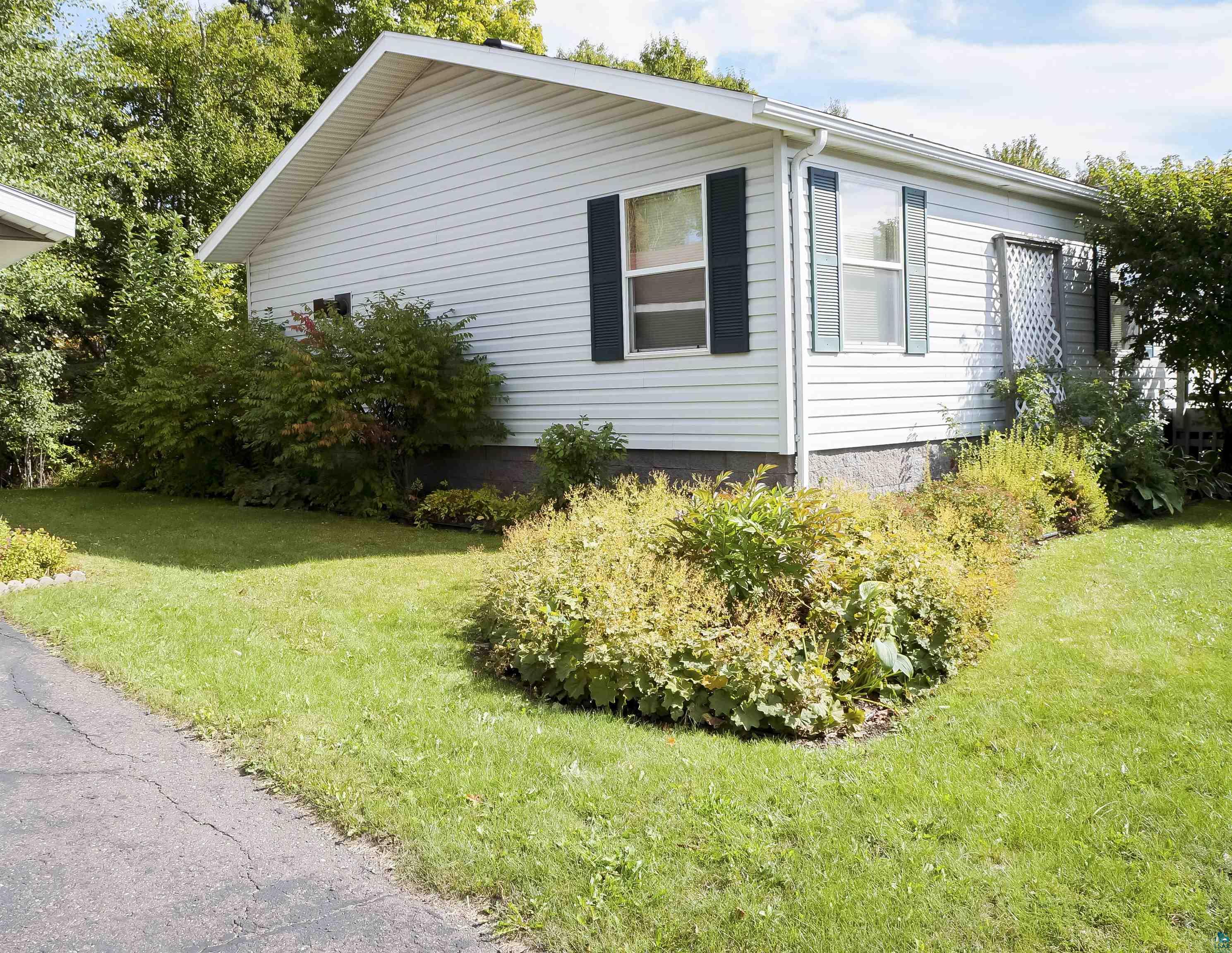 White-sided house with dark shutters beside a landscaped lawn and flower beds.